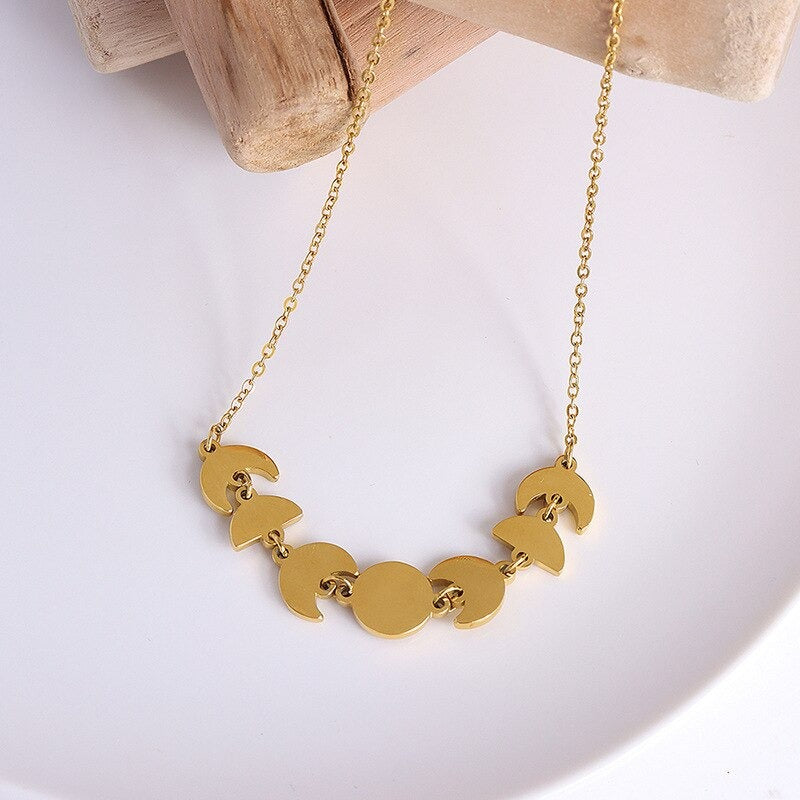 A picture of a Gold Moon Phase Necklace laying on a piece of wood over a white background.