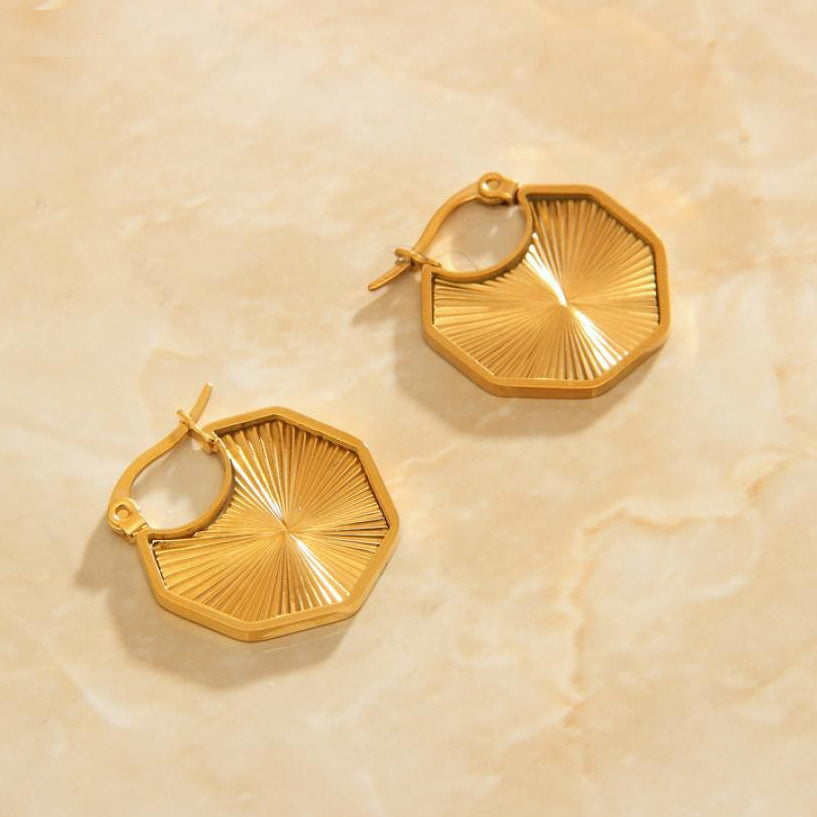 Gold Octagon Sun Earrings laying on a rose quartz surface.