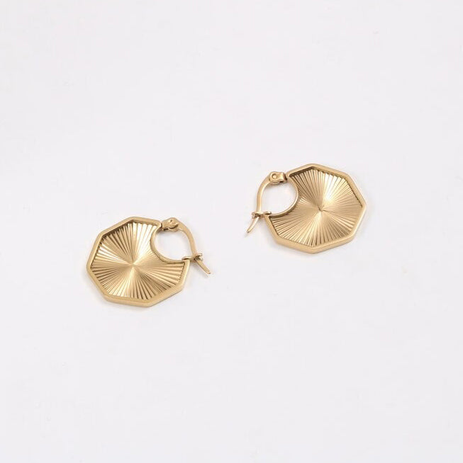 Gold Octagon Sun Earrings laying on a smooth white surface.