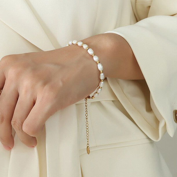 A close up photo of a woman with a cream coloured suit wearing the minimalist gold freshwater pearl chain link bracelet.
