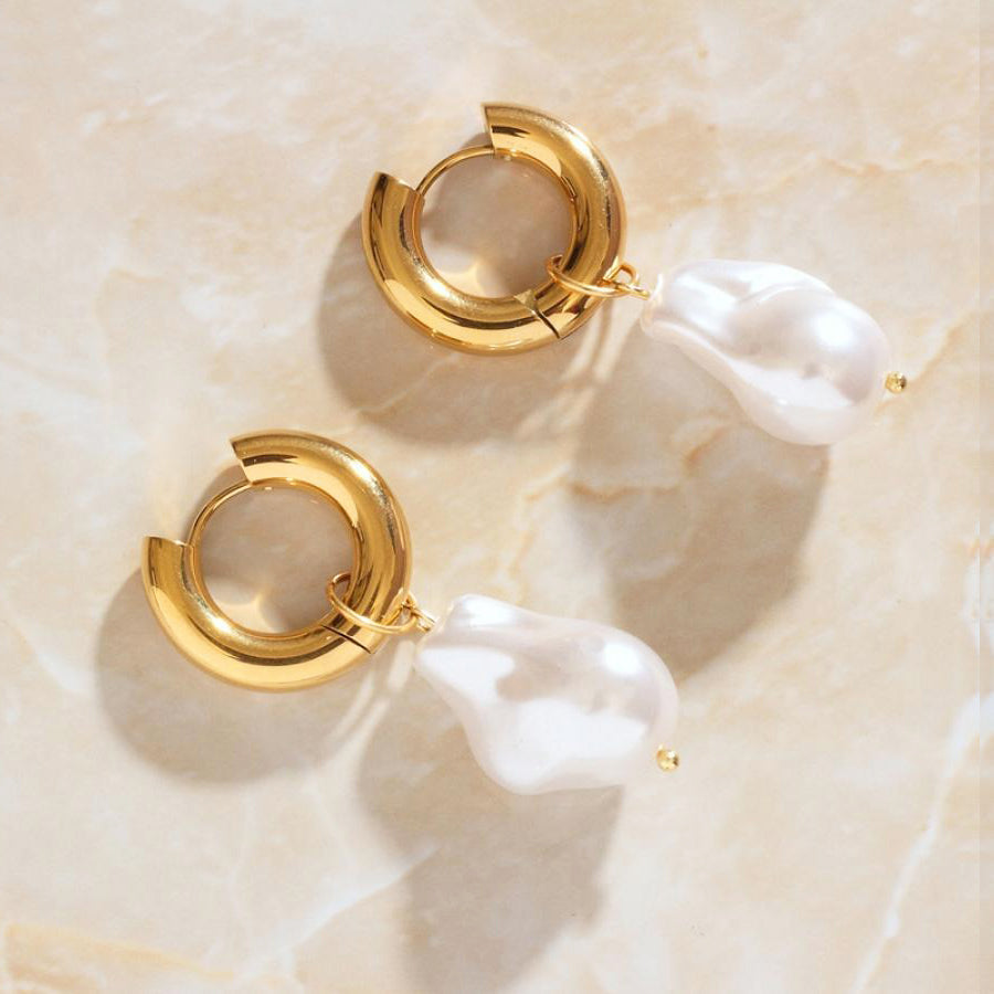 Gold Pearl Hoop Earrings laying on a smooth rose quartz surface shining brightly.