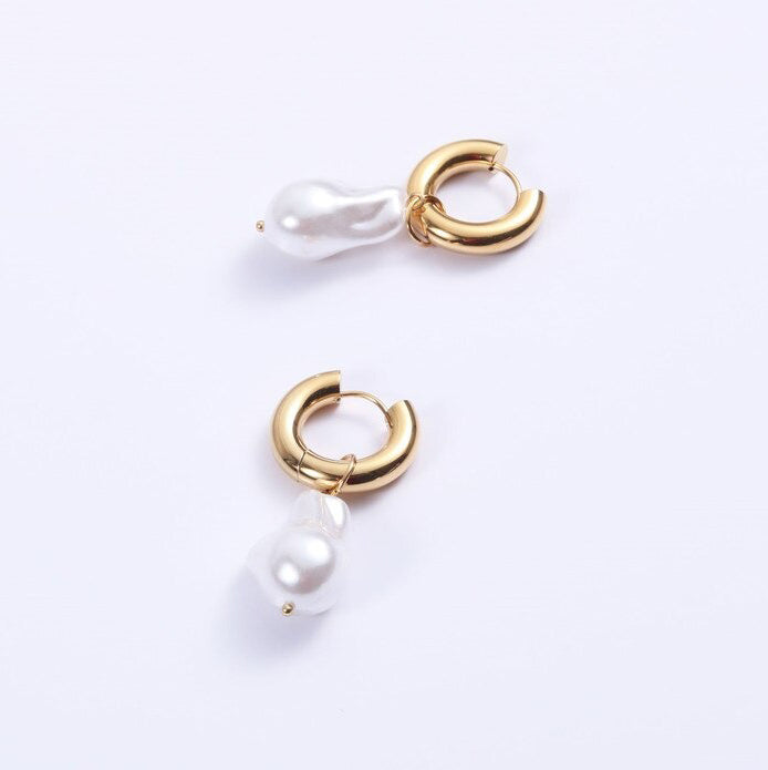 Gold Pearl Hoop Earrings laying on a white surface shining brilliantly.