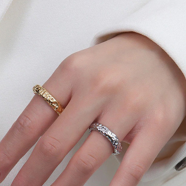 A ladies hand wearing a gold ring with a stone pattern and a silver ring with a stone pattern.