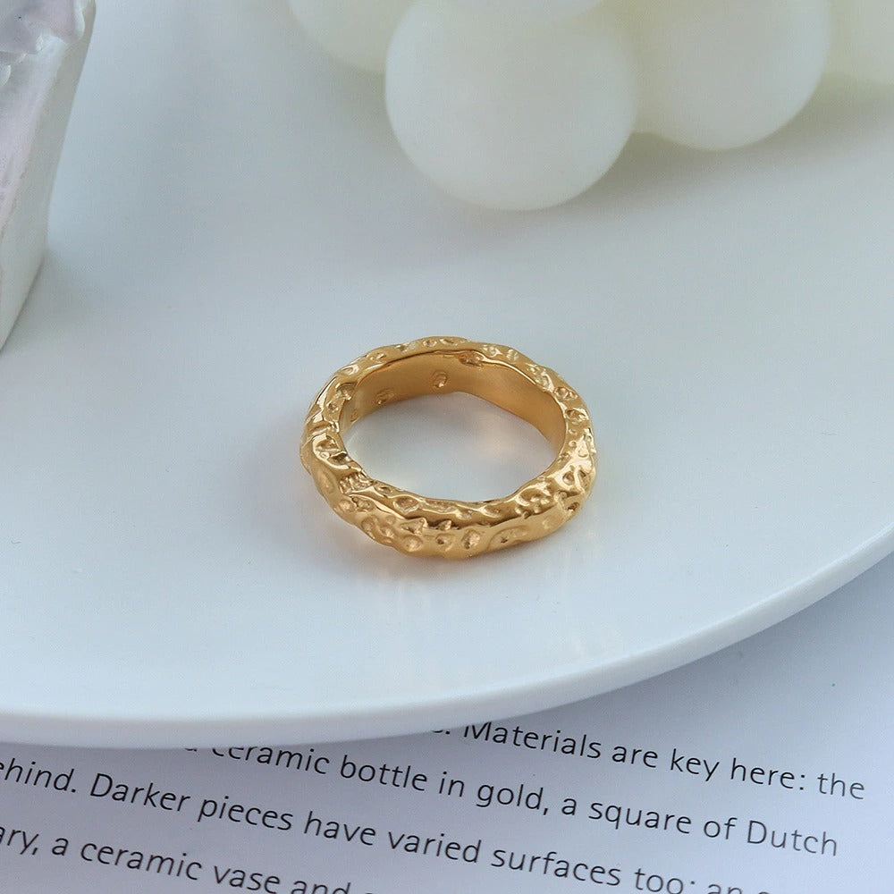 A gold ring with a stone pattern on a white dish sitting on top of a newspaper.