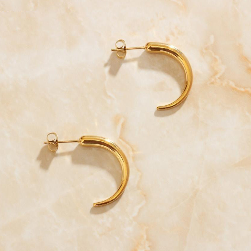 Gold Pipa Chilli Earrings laying on a smooth rose quartz surface shining brightly.