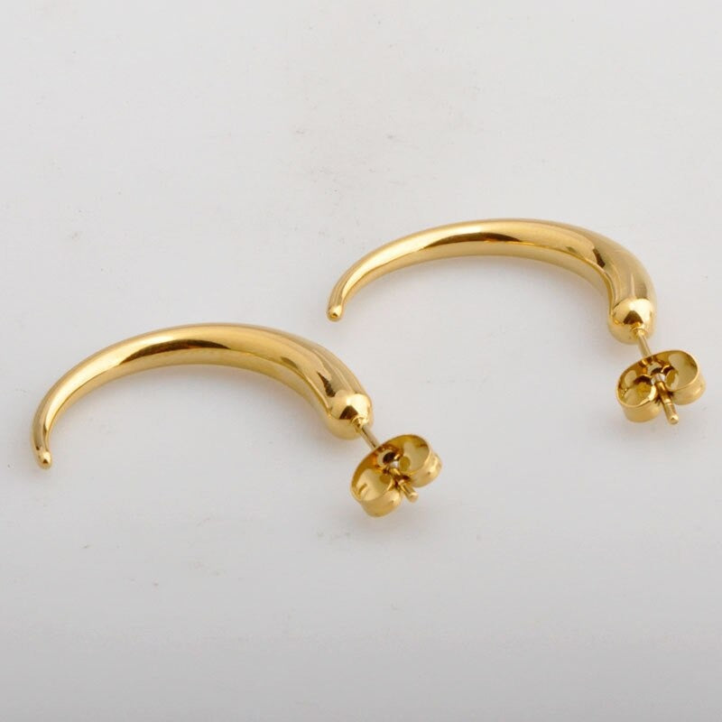 Gold Pipa Chilli Earrings laying on a smooth white surface shining brightly.