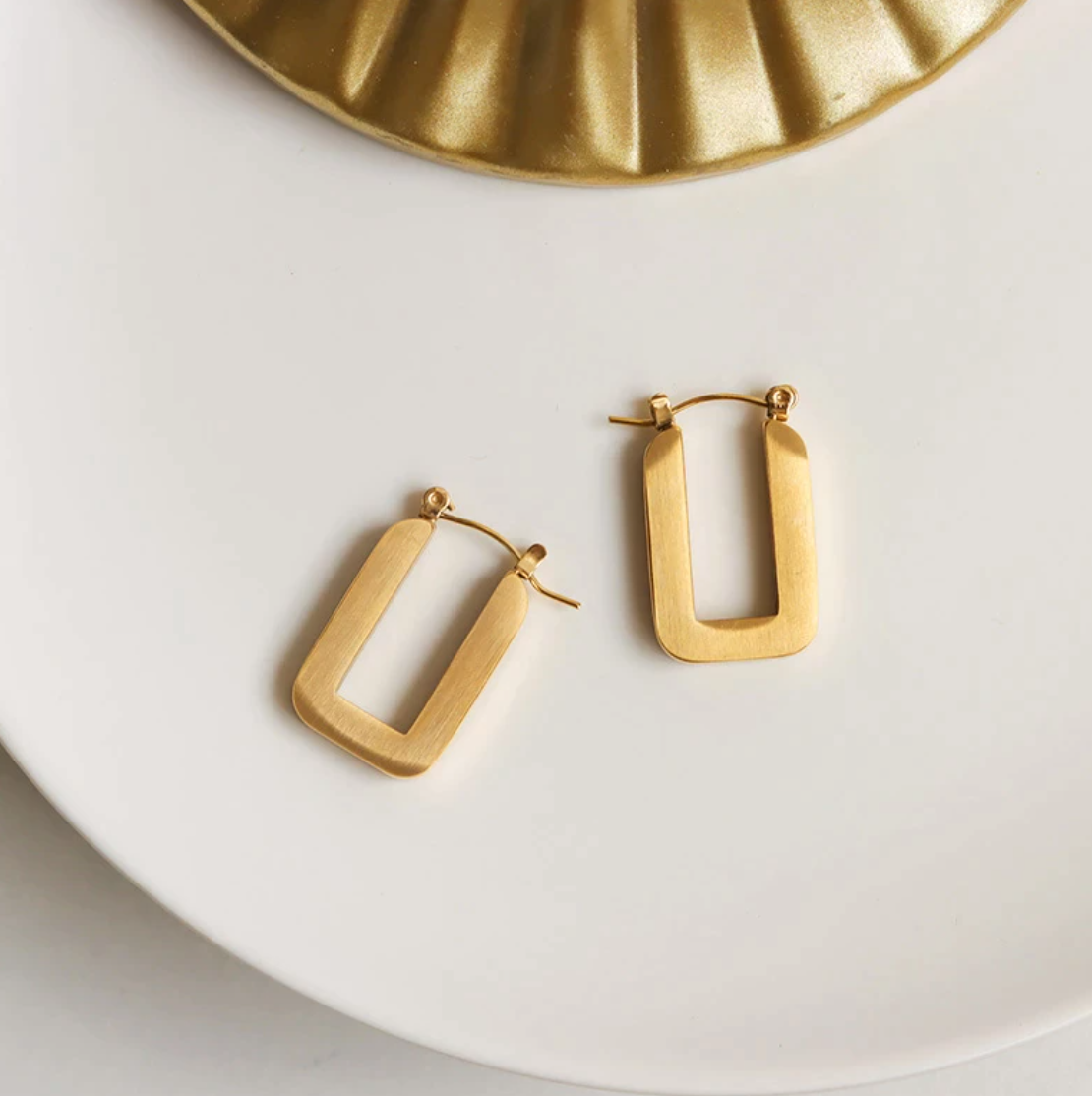 Gold Rectangular You Earrings laying on a smooth white surface.