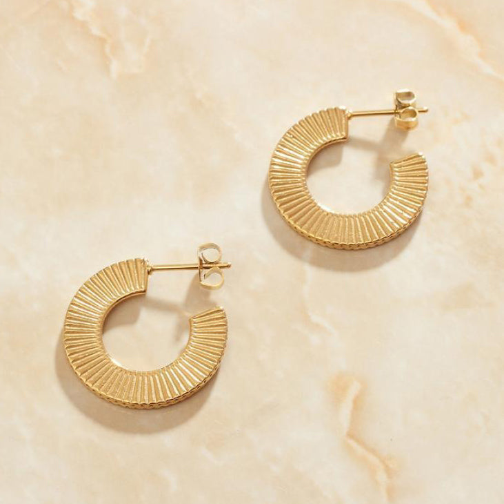 Gold Ribbed Curved Earrings laying on a smooth rose quartz surface shining brightly.