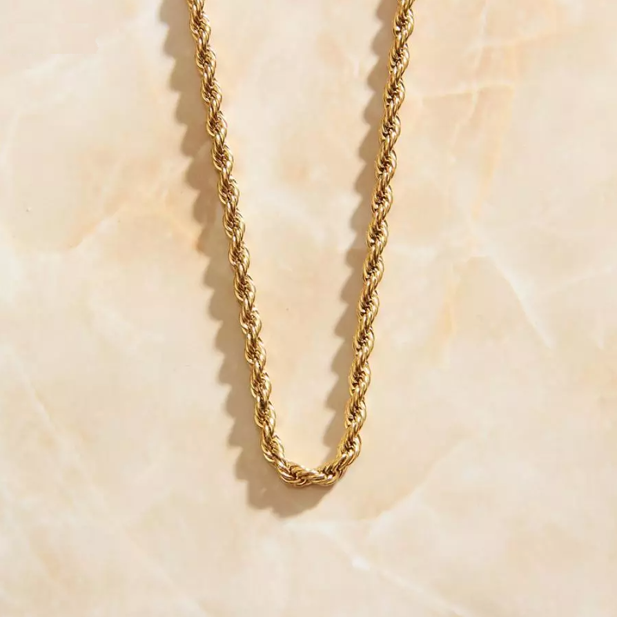 A simple yet elegant Gold Rope Chain Necklace hanging over a marbled peach coloured background.