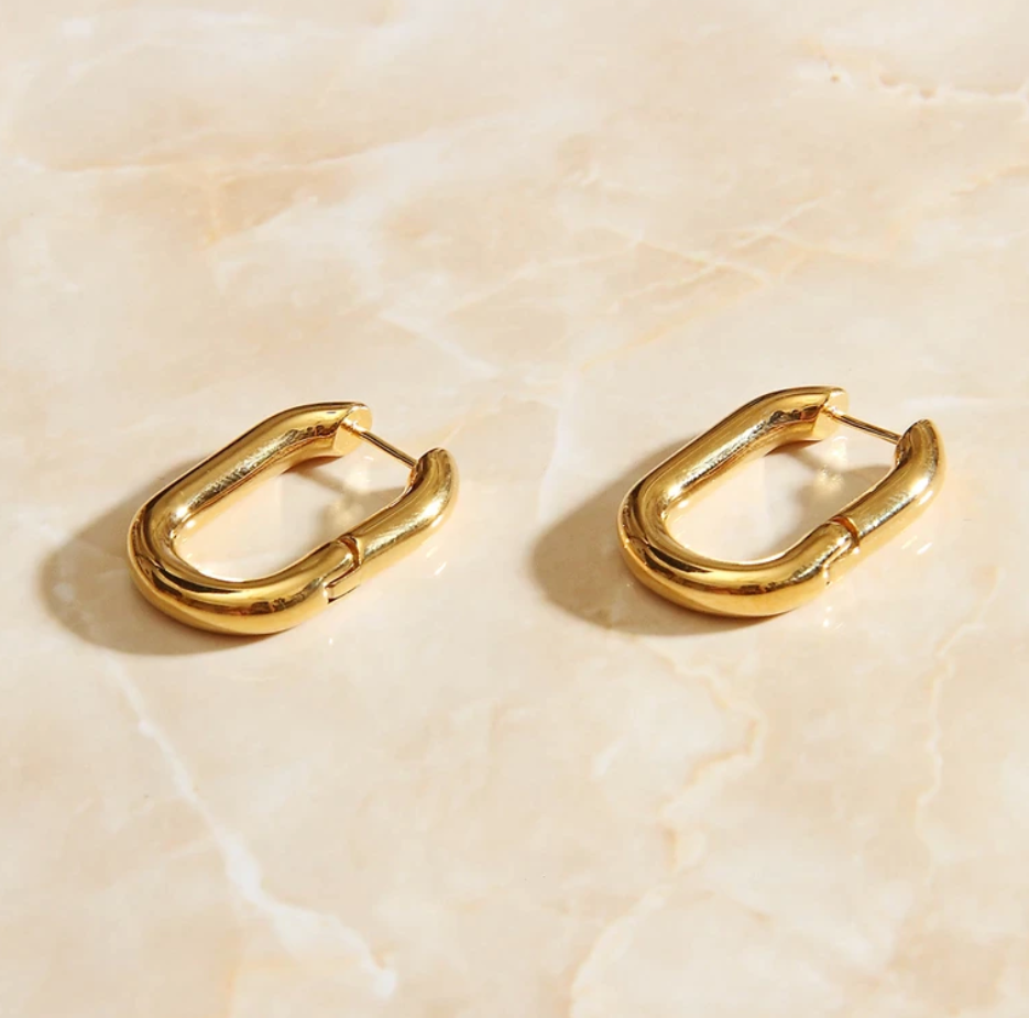 Gold Rounded Oval Earrings laying on a smooth rose quartz surface shining brightly.