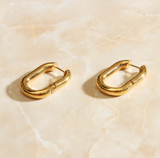 Gold Rounded Oval Earrings laying on a smooth rose quartz surface shining brightly.