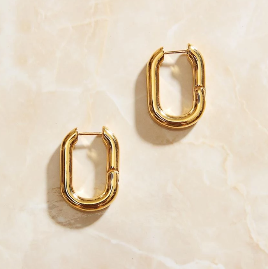 Overhead photograph of Gold Rounded Oval Earrings laying on a rose quartz surface.