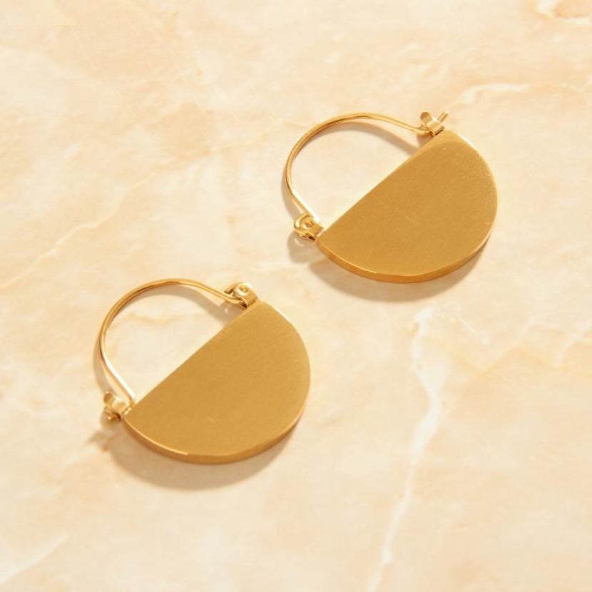 Gold Semi Circle Earrings laying on a peach coloured marble background.