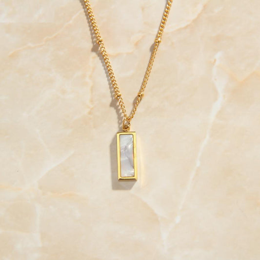 Gold Shell Rectangle Pendant Necklace laying on a minimal marble background.