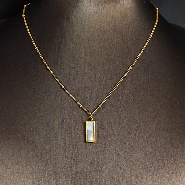 Gold Shell Rectangle Pendant Necklace hanging on a black mannequin. 