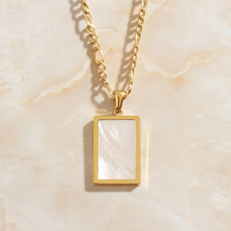 A Gold Shell Square Pendant Necklace shining on a marbled peach coloured background.