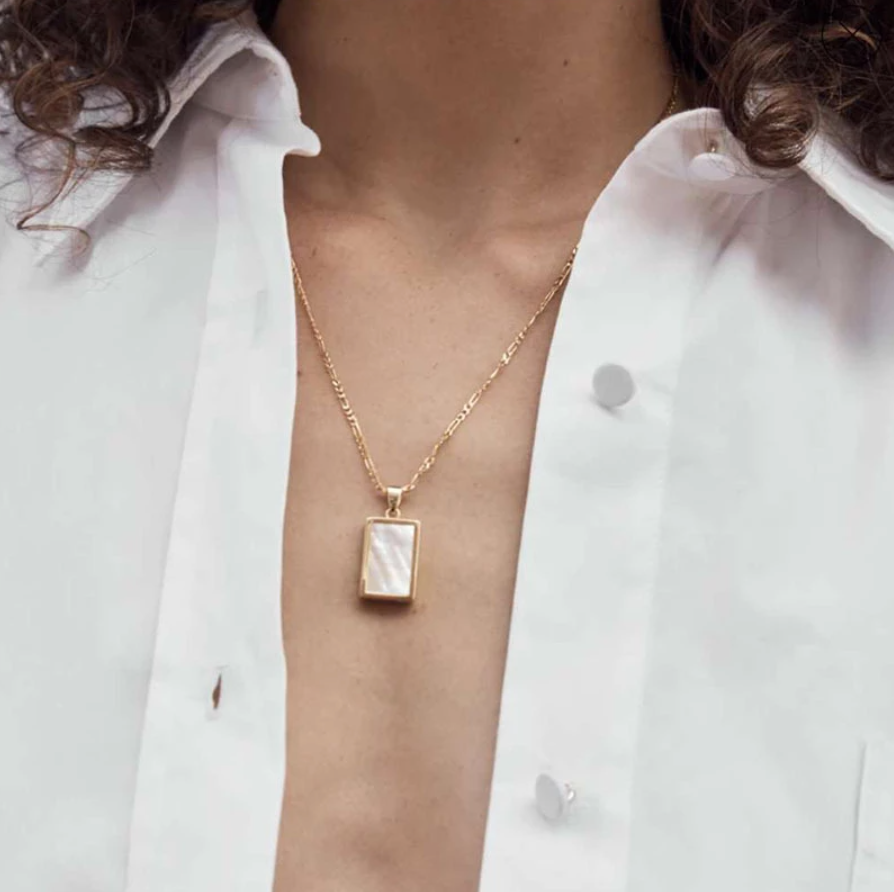 Gold Shell Square Pendant Necklace hanging on a brunette woman's neck with a white open shirt.