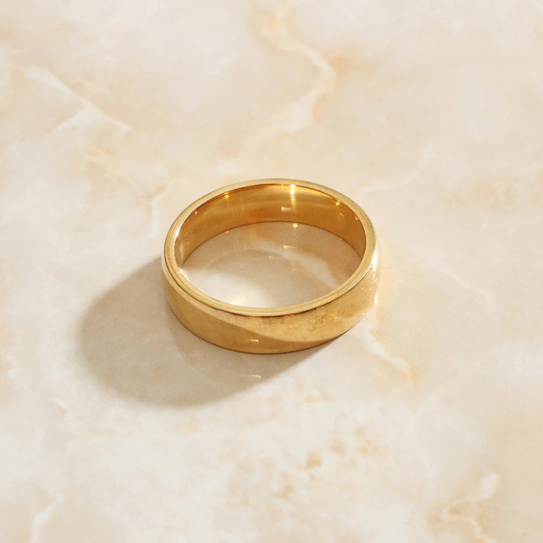 A simple gold band laying on a peach coloured marble surface.