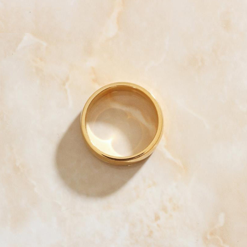 A simple minimalist gold ring on a sleek marble background.