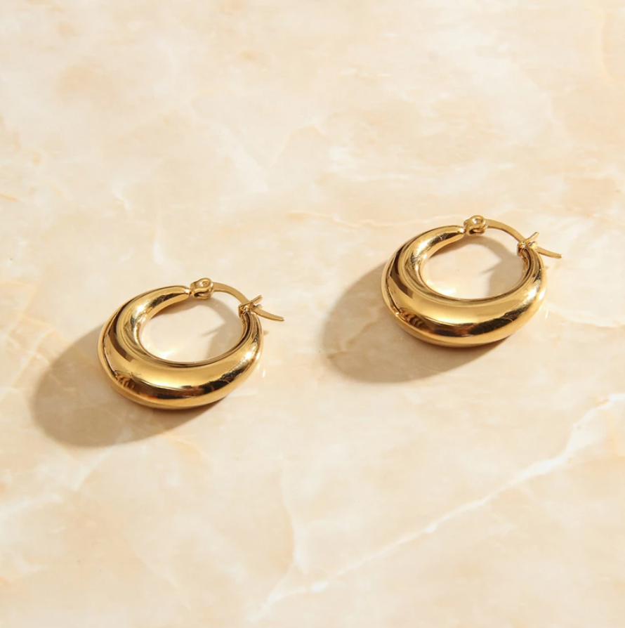 Gold Smooth Curved Earrings laying on a smooth rose quartz surface shining brightly.