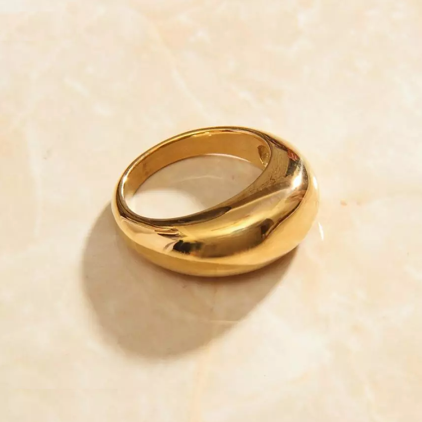 Gold Smooth Curved Signet Ring with a radiant shine, laying on a marble surface.