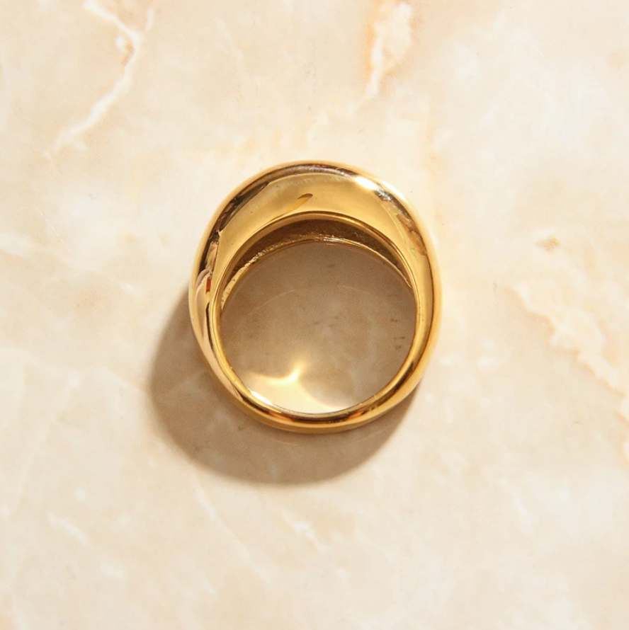 A beautiful minimal curved signet ring laying on a smooth marble surface.