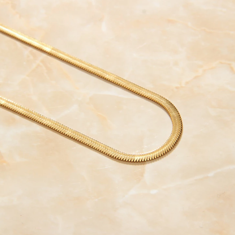 A Gold Snake Chain Necklace presented in a diagonal fashion on a marbled background.