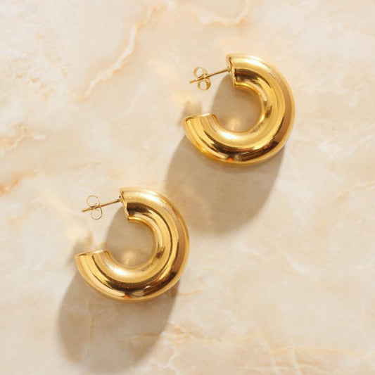Gold Solinas Hoop Earrings sitting on a marbled background bathed in sunlight.