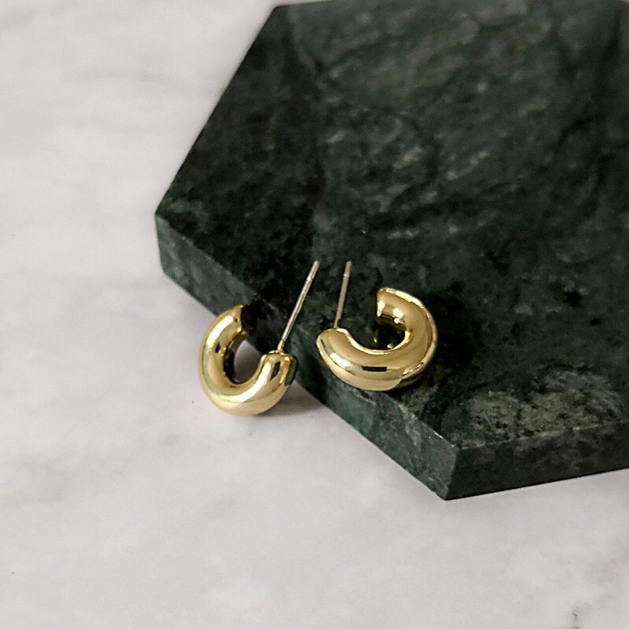 Gold Solinas Hoop Earrings sitting on a dark marbled surface, shining brightly.