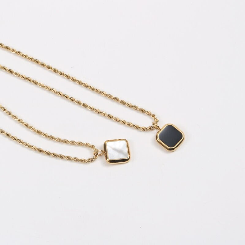 Both black and white set square pendant necklaces laying on a white background.