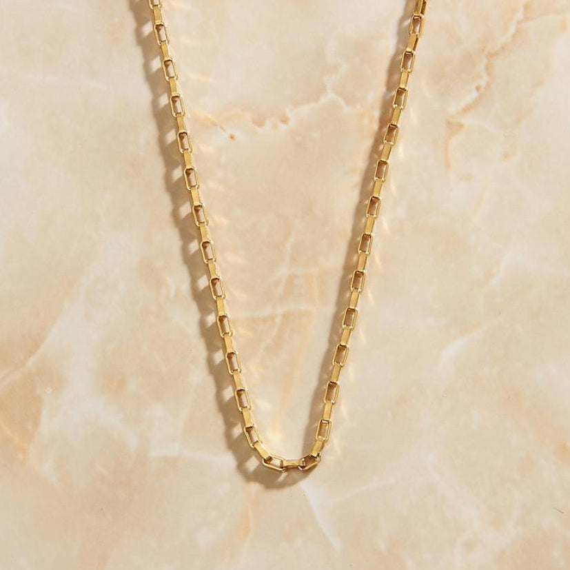 Gold Square Box Chain Necklace laying on a marbled peach apricot coloured background.