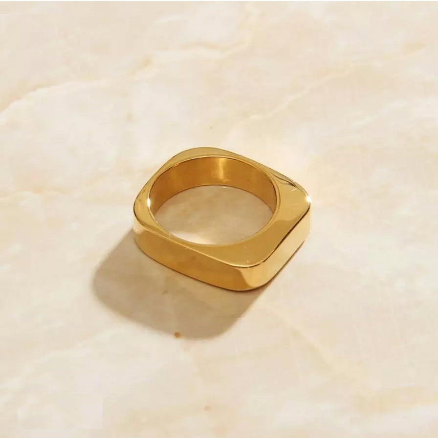 A gold square signet ring laying on a marble surface.