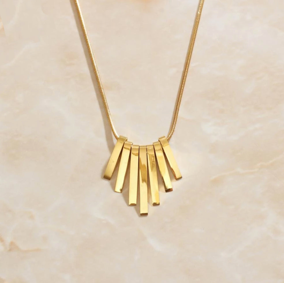 Gold Stalactite Pendant Necklace on thin snake chain laying on a marbled background.