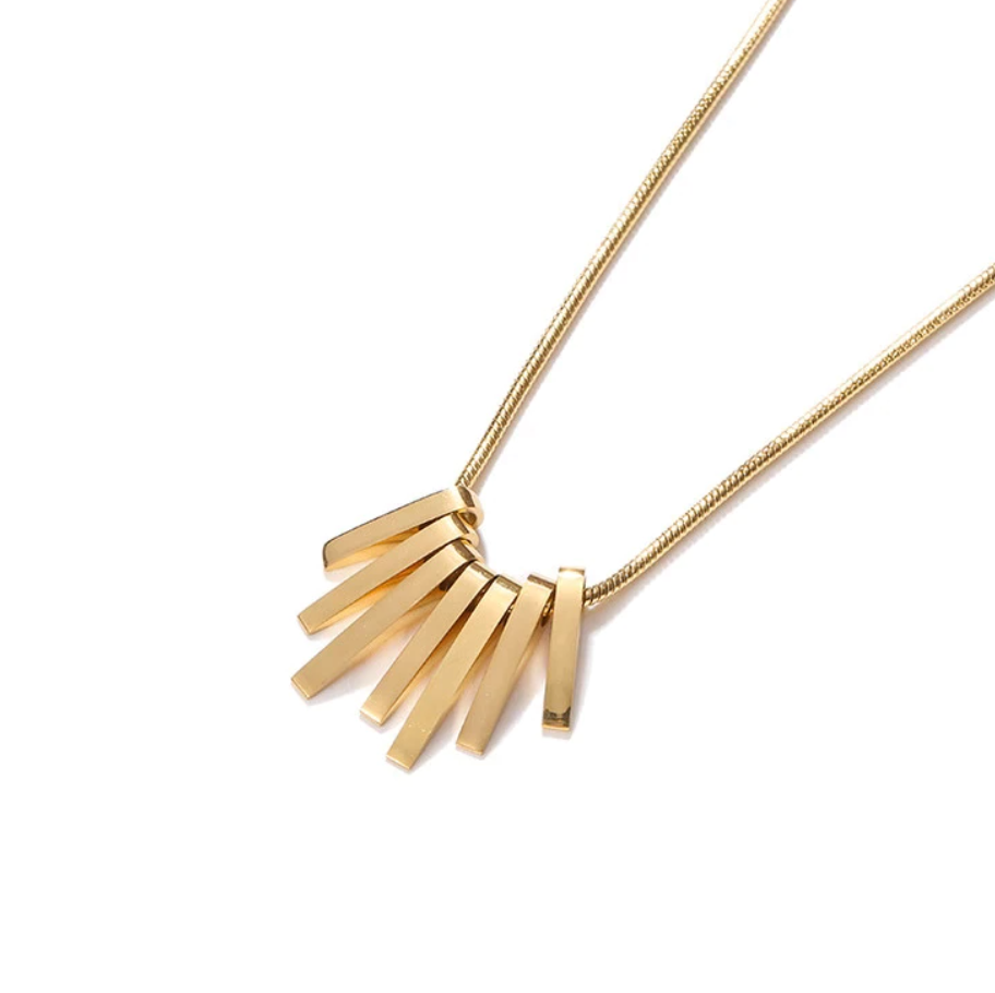 A closeup of the Gold Stalactite Pendant Necklace laying diagonally on a white background.