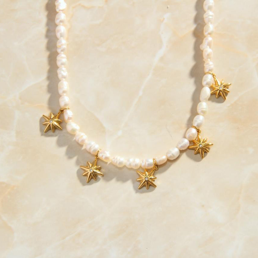 Gold Pearl Necklace with five Star Charms presented on a marbled background.