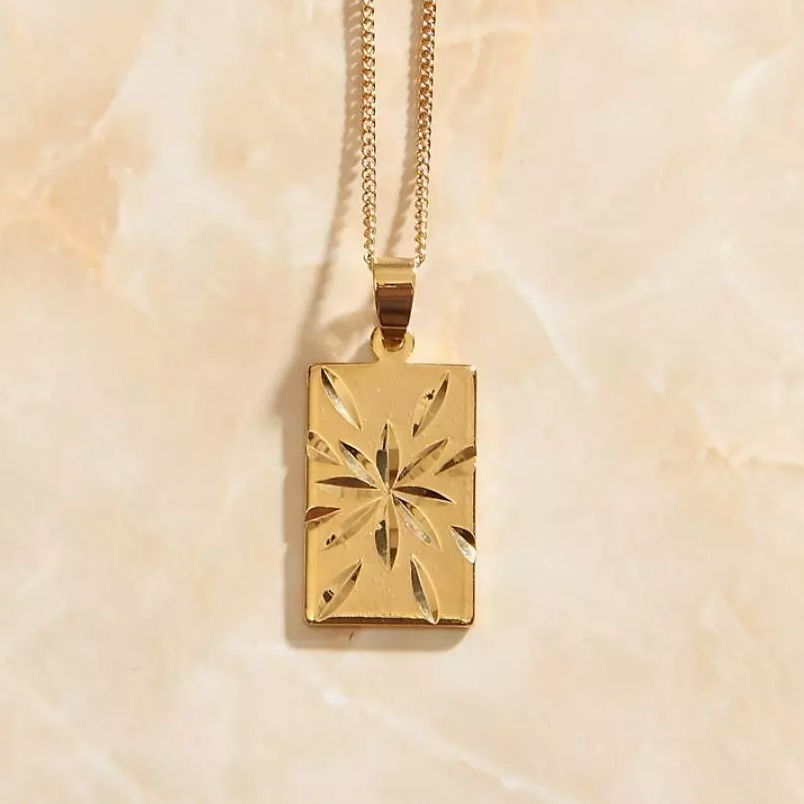 Closeup shot of Gold Starburst Pendant Necklace shining brightly on a marbled background.