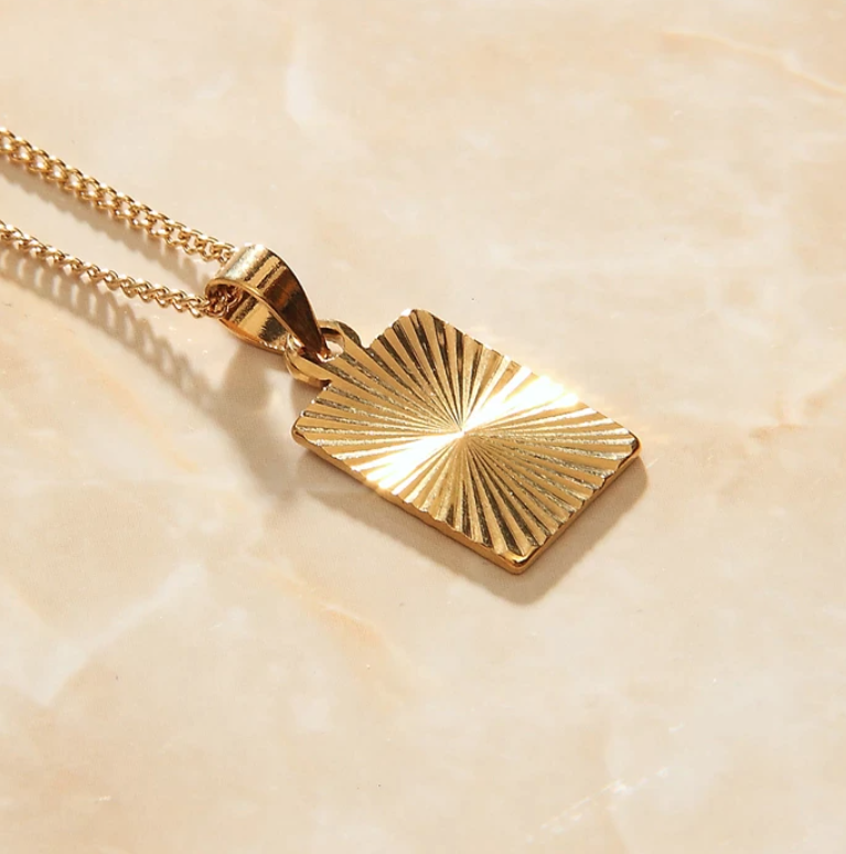 Golden Sunburst Style Patterned Pendant shining brightly on marble surface.