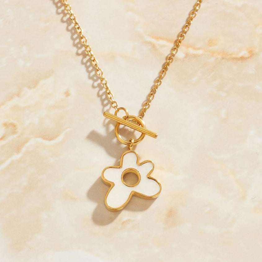 A Gold T-bar Necklace with White Flower Enamel Pendant bathed in warm sunlight.