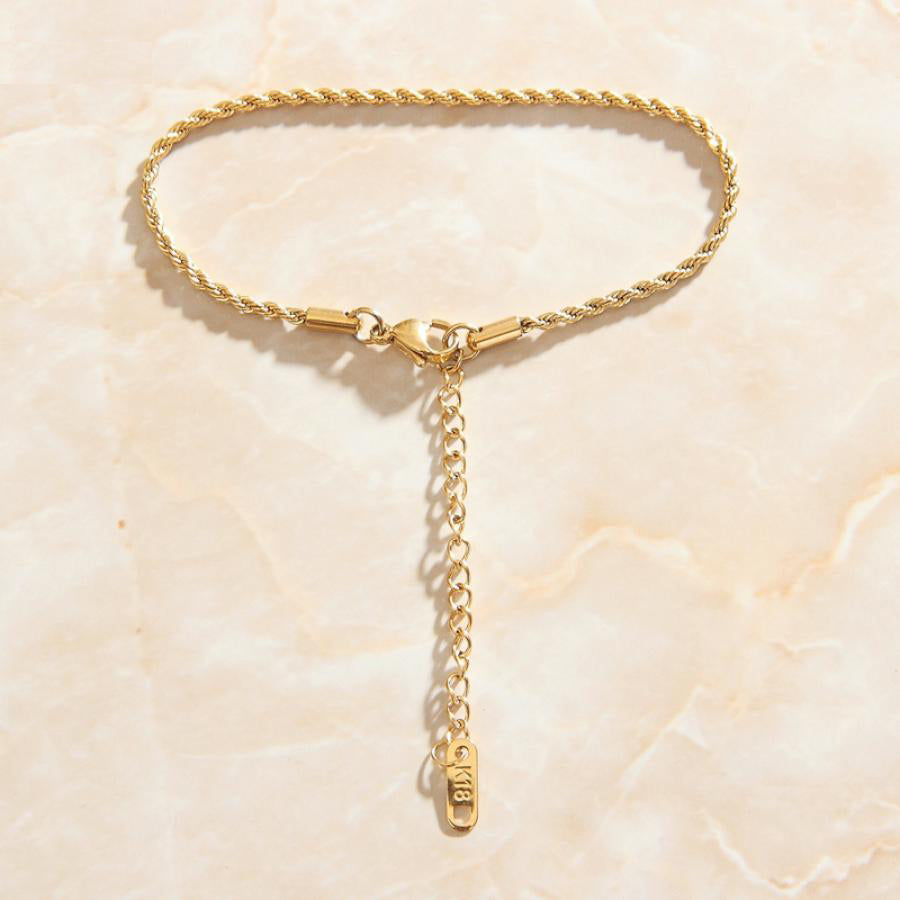 A smooth quartz surface with a Gold Thin Rope Chain Link Bracelet laid on top of it.