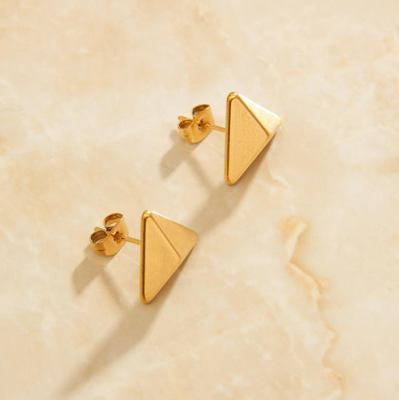 Gold Trigoni Polygon Earrings sitting on a marbled background bathed in sunlight.