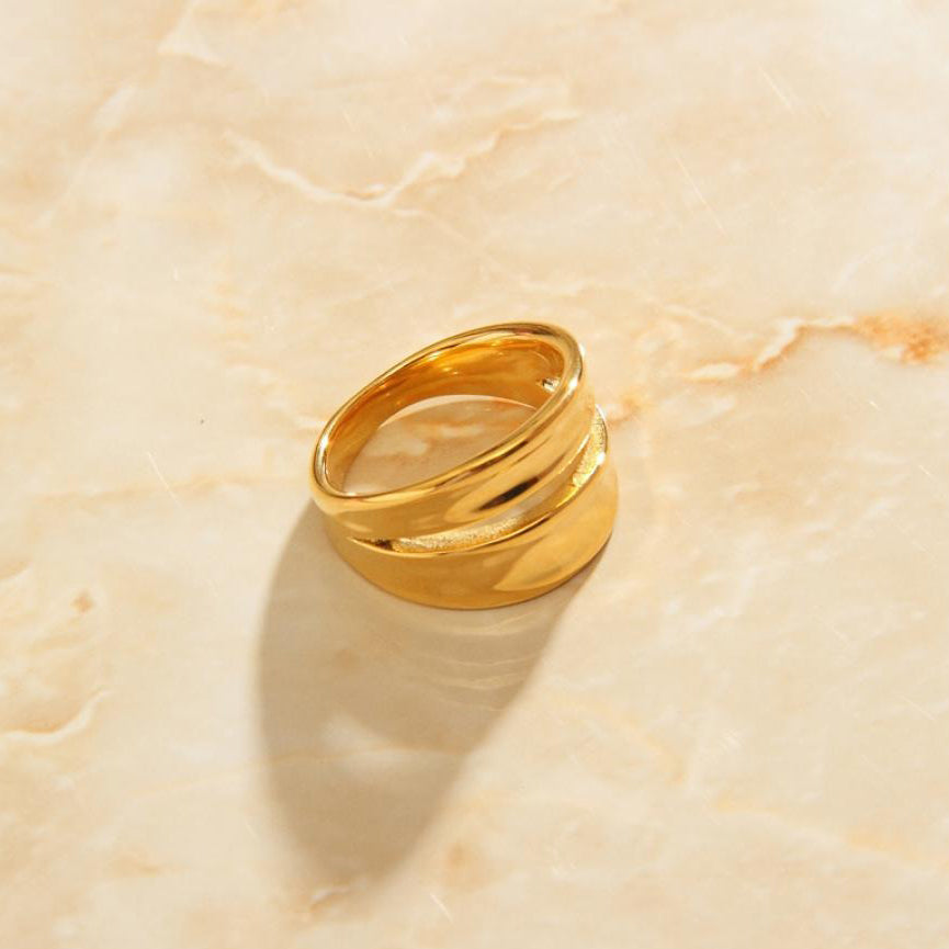 A beautiful Gold Twin Split Signet Ring on a smooth apricot coloured quartz background.