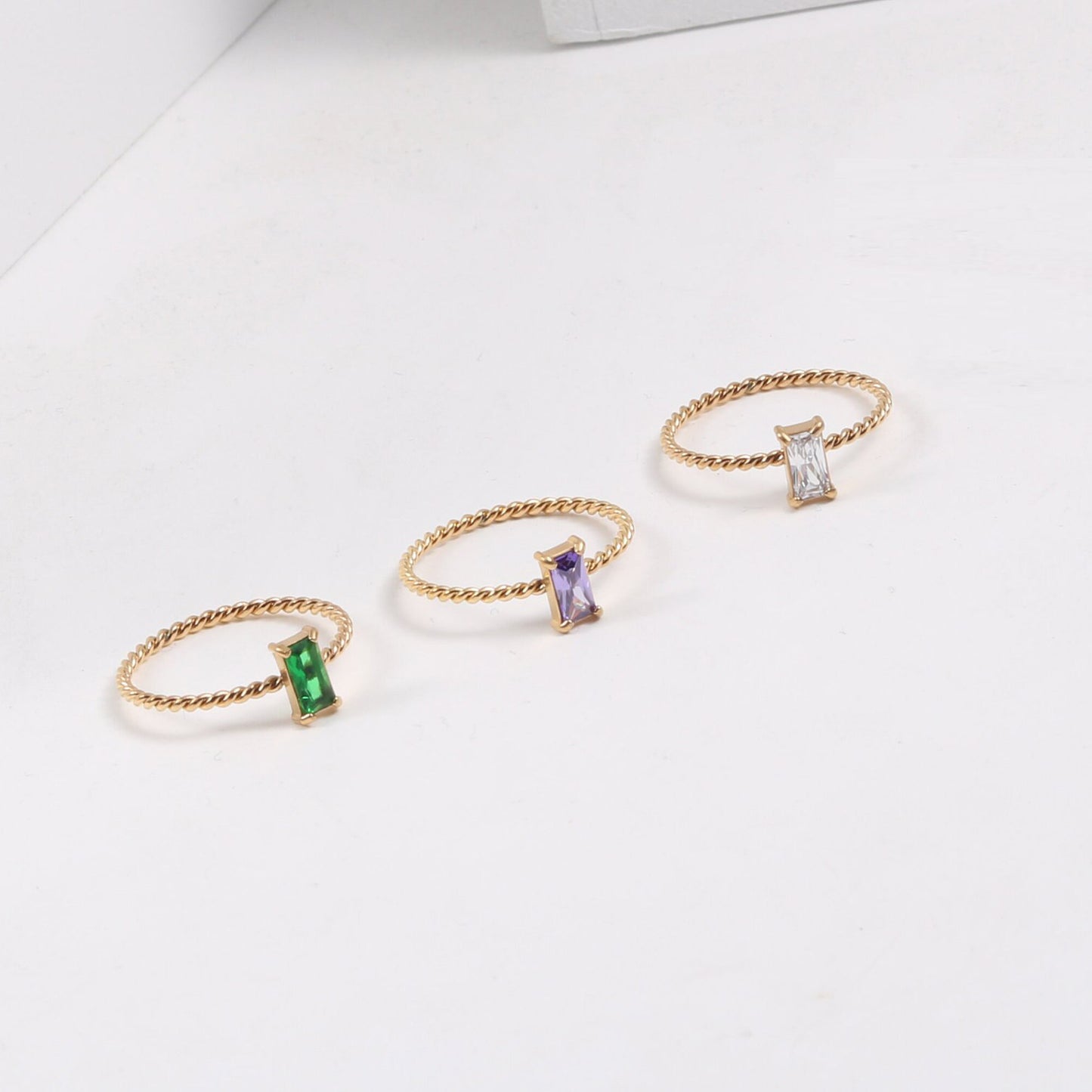 Three Gold Twist Cubic Zirconia Rings each a different colour on a white surface.