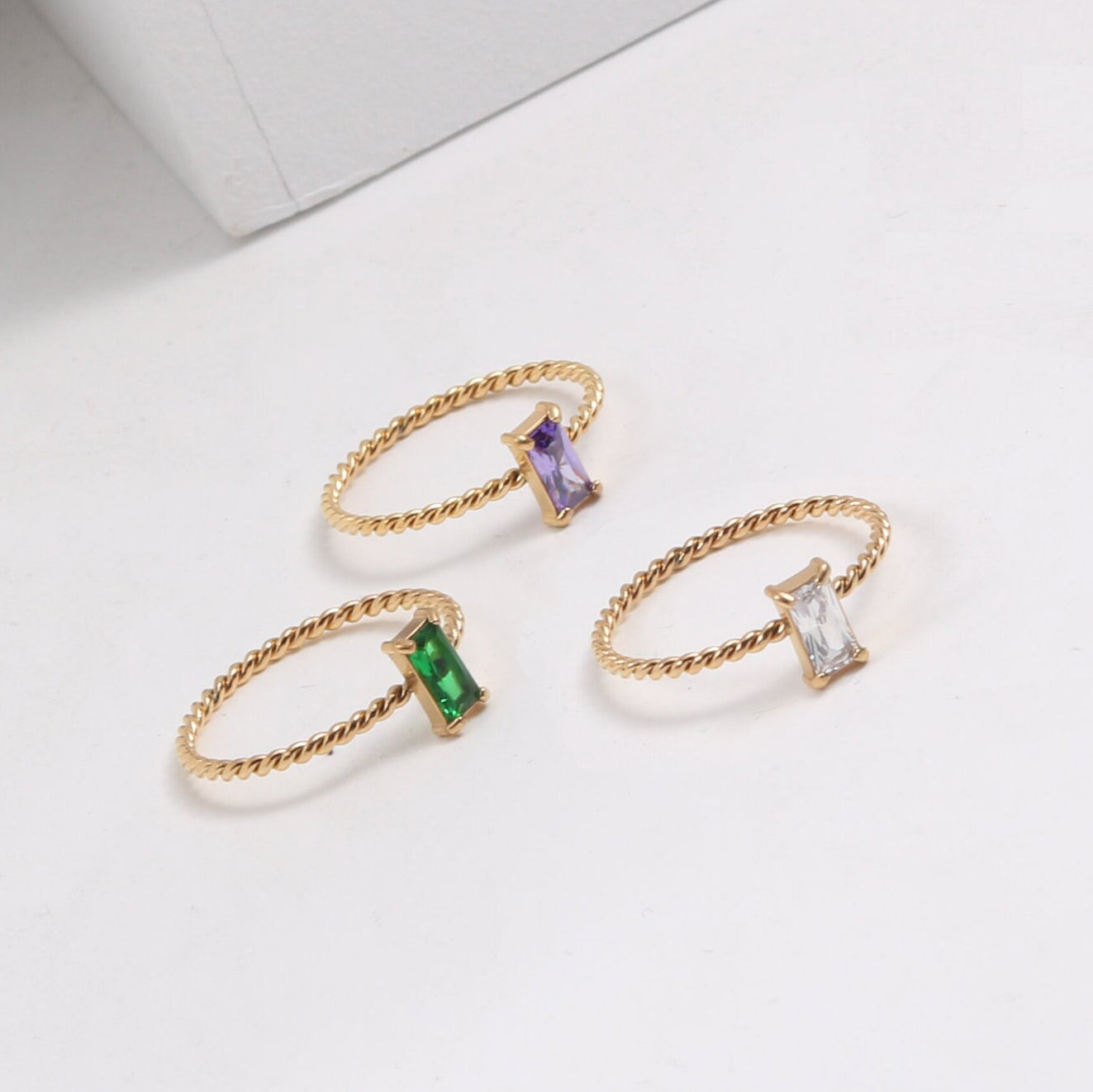 Three Gold Twist Cubic Zirconia Rings each a different colour on a white surface.