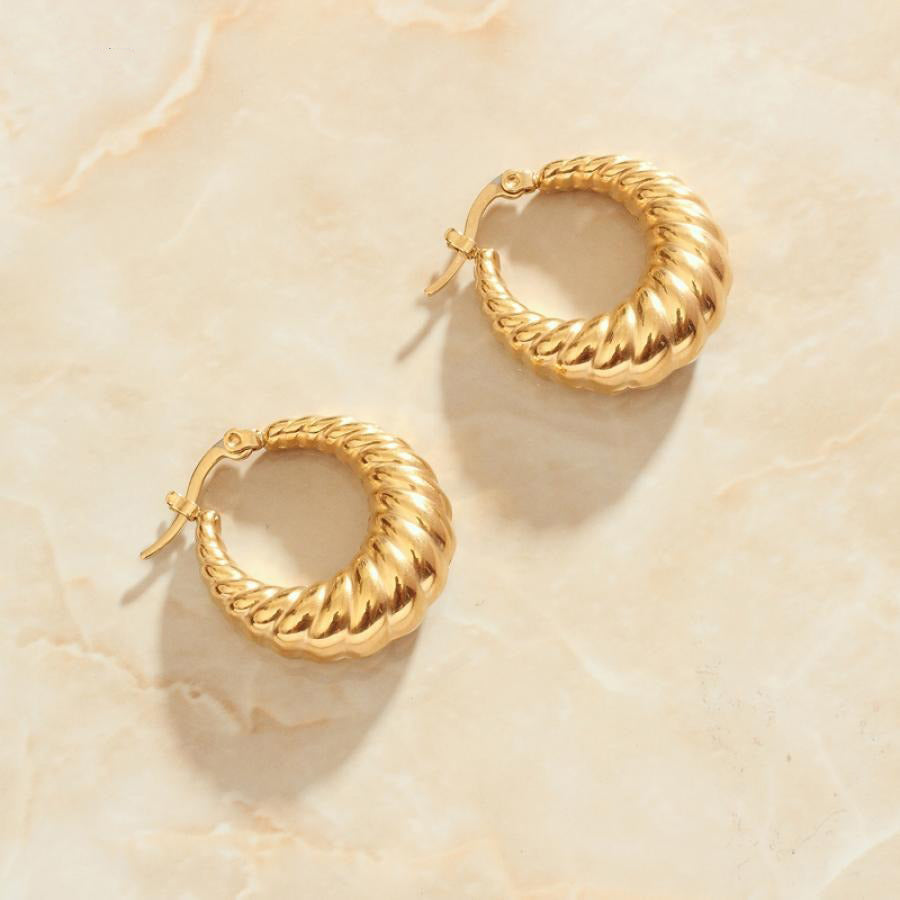 Gold Twist Earrings sitting on a marbled background bathed in sunlight.