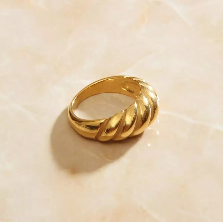 Gold Twist Signet Ring sitting on a peach coloured quartz background.