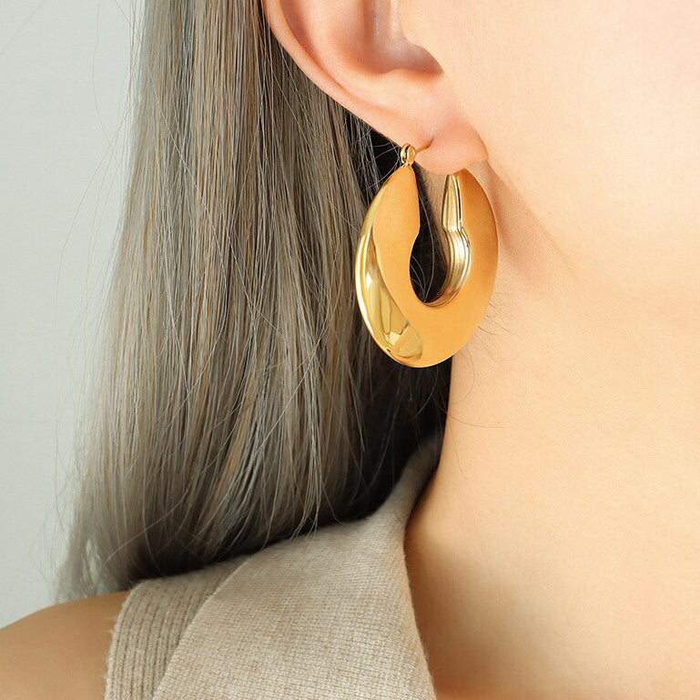 Gold Wide Polished Hoop Earrings shining brightly whilst being worn by a beautiful woman with blonde hair.
