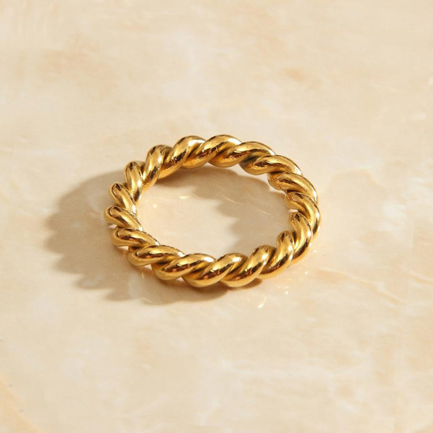 Gold wound twine signet ring sitting on a marbled background bathed in sunlight.