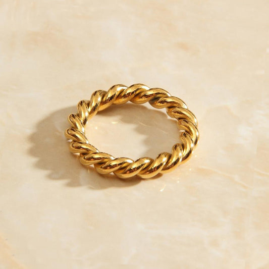 Gold wound twine signet ring sitting on a marbled background bathed in sunlight.