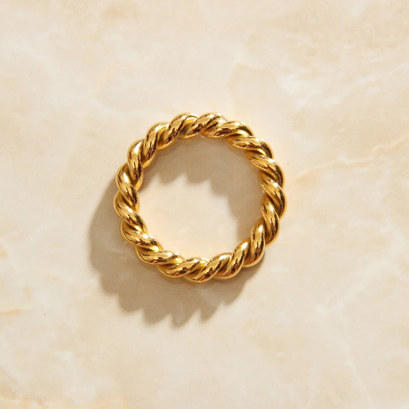 Gold wound twine signet ring sitting on a marbled background bathed in sunlight.