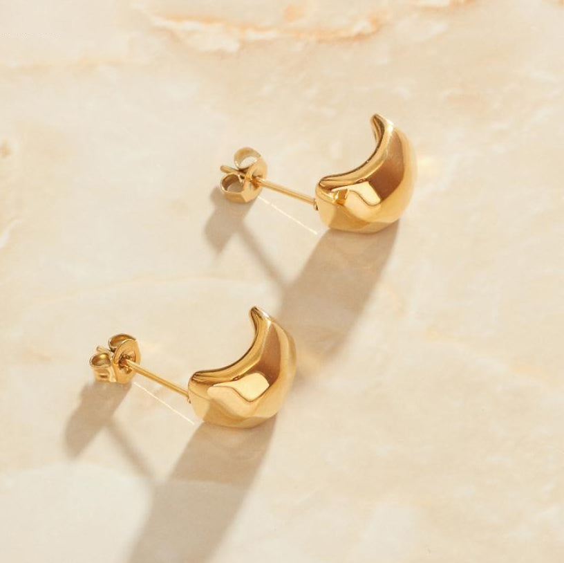 Gold Zani Faceted Earrings laying on a smooth rose quartz surface shining brightly.